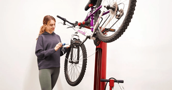 A woman is holding a bicycle chain while standing next to a bicycle on a red stand.